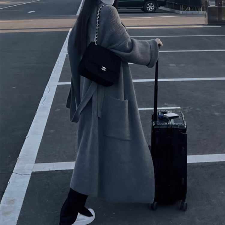 a woman wearing a hat and a long coat with a suitcase