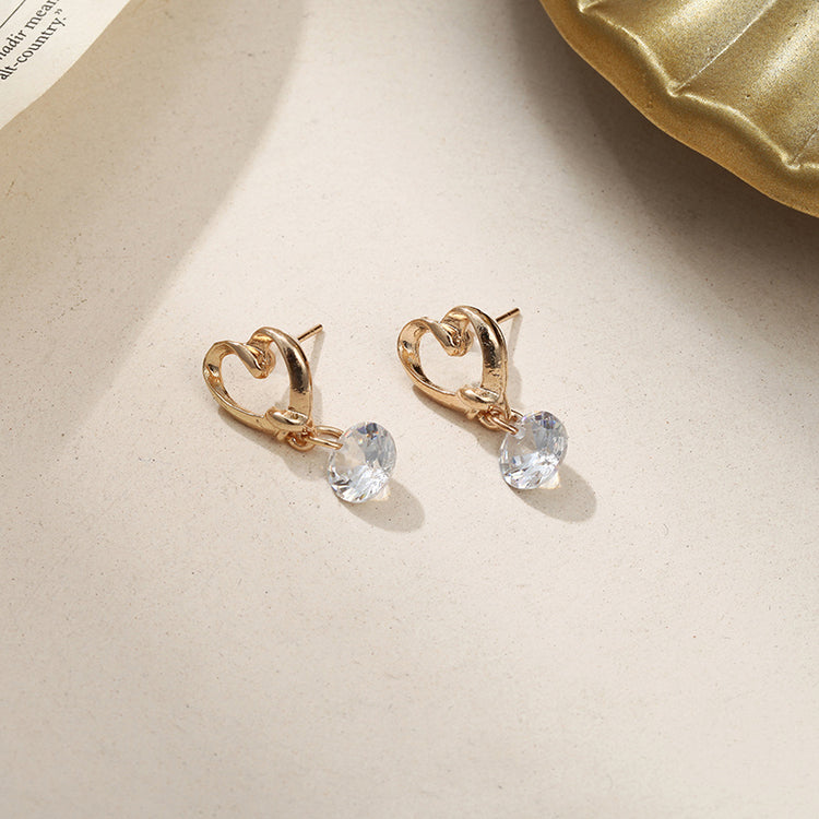 a pair of gold earrings with a heart shaped stone