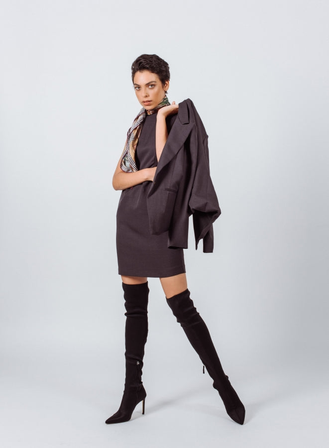 a woman in a dress and over the knee boots holding a jacket over her shoulder