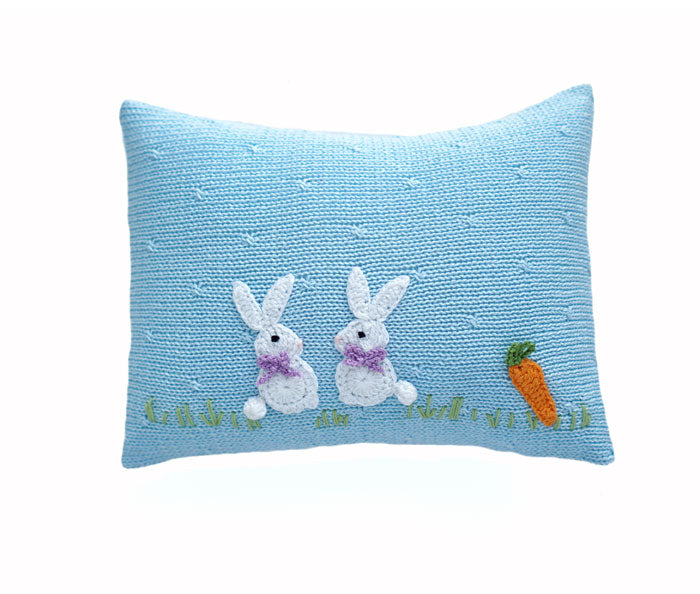 a blue pillow with two rabbits and a carrot