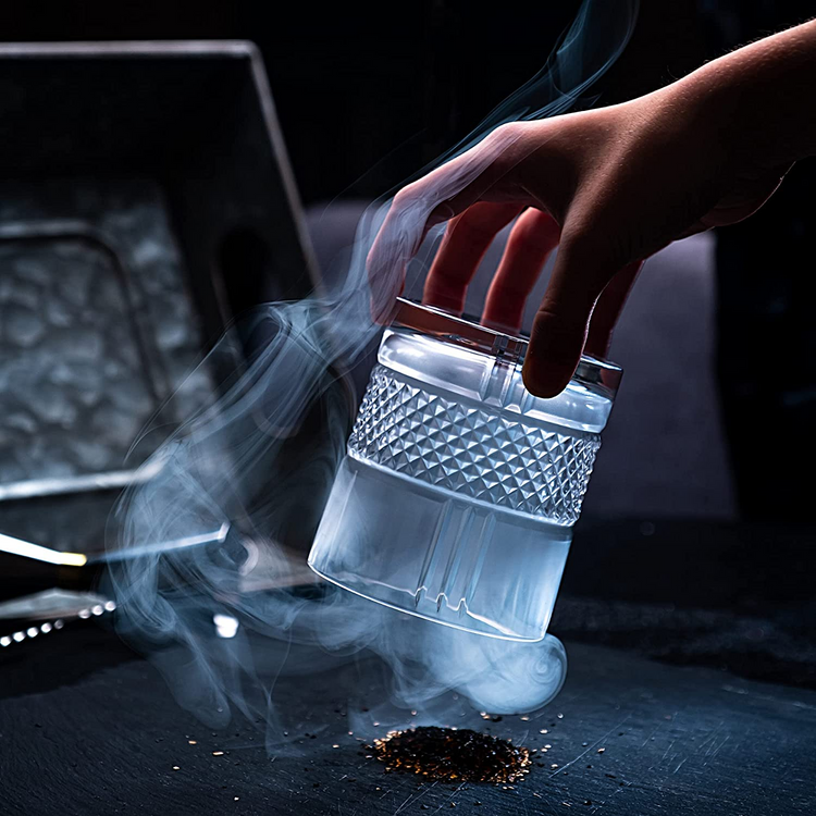 a hand holding a glass with smoke coming out of it