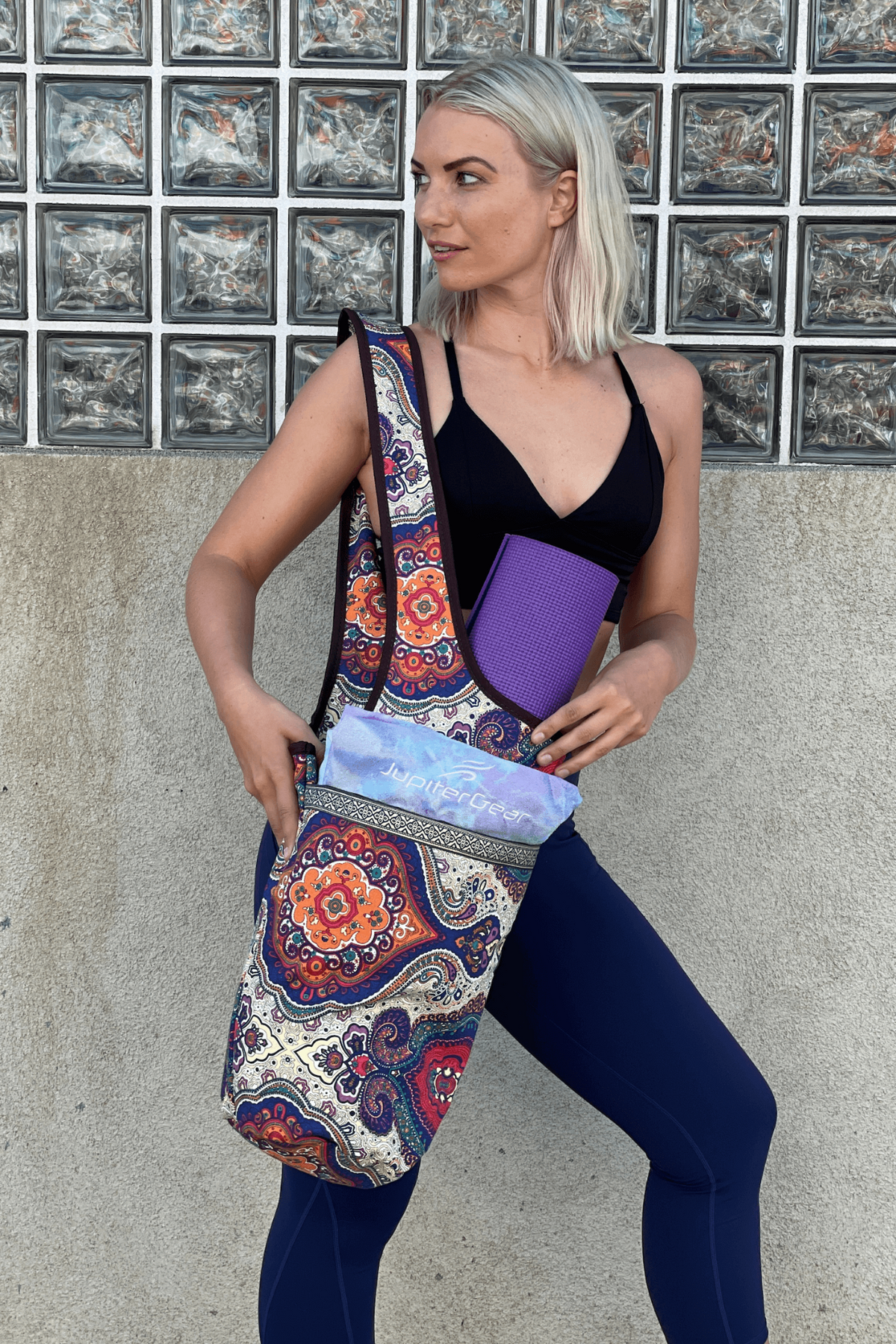 a woman in a black tank top and blue leggings holding a yoga mat