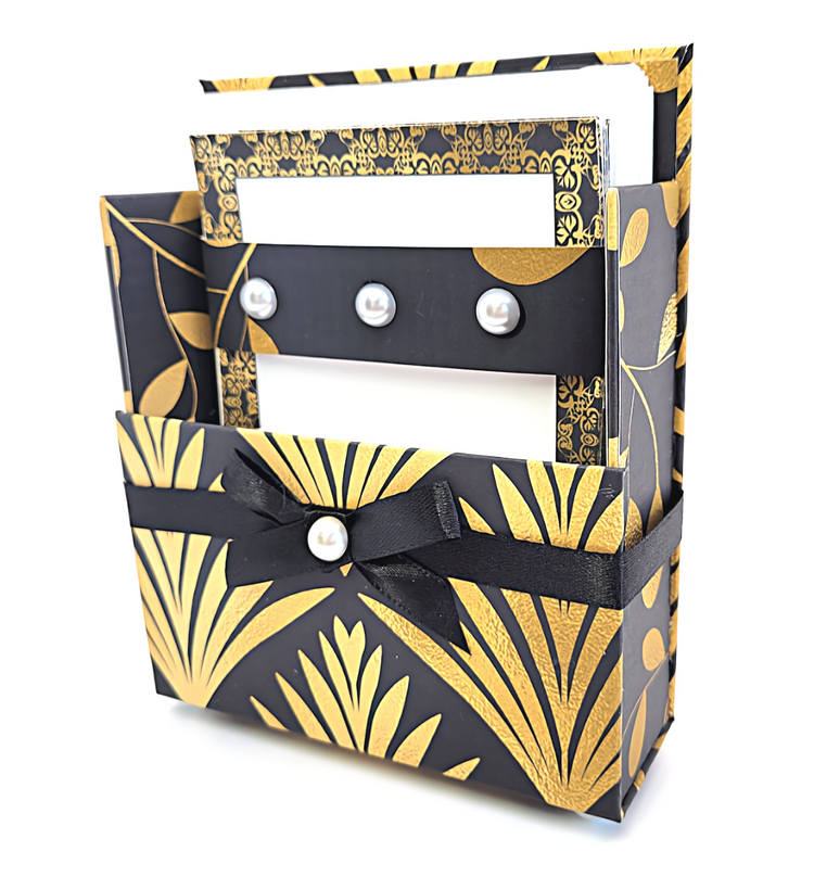 a black and gold box with a black ribbon and white paper
