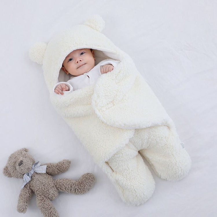 a baby wrapped in a blanket next to a stuffed bear