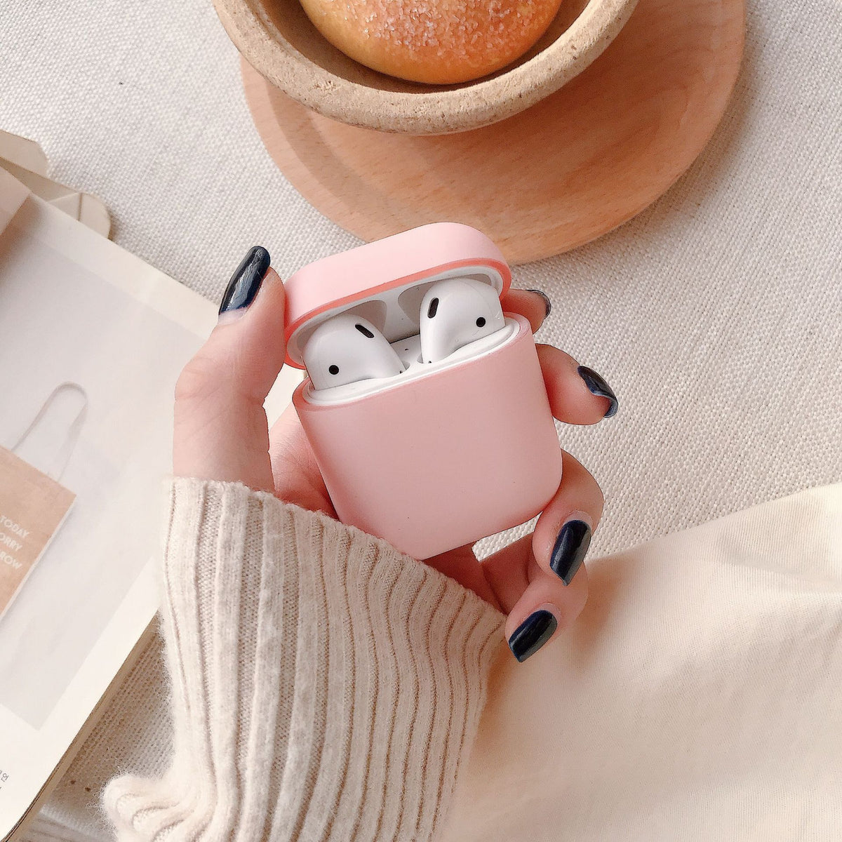 a hand holding a pink case with white earbuds
