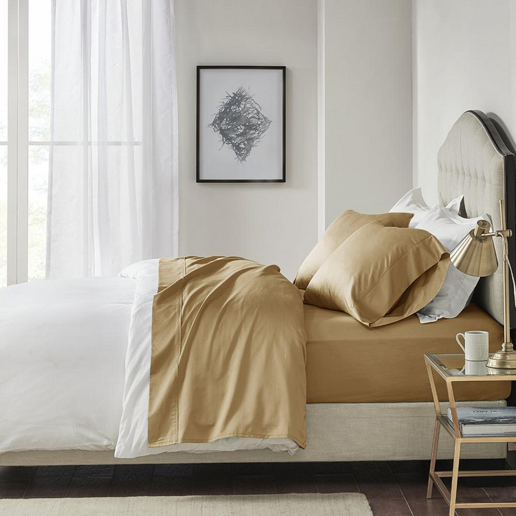 a bed with a gold sheet and a lamp