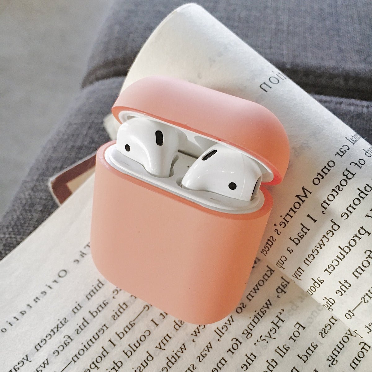 a pink case with white earbuds in it on a book
