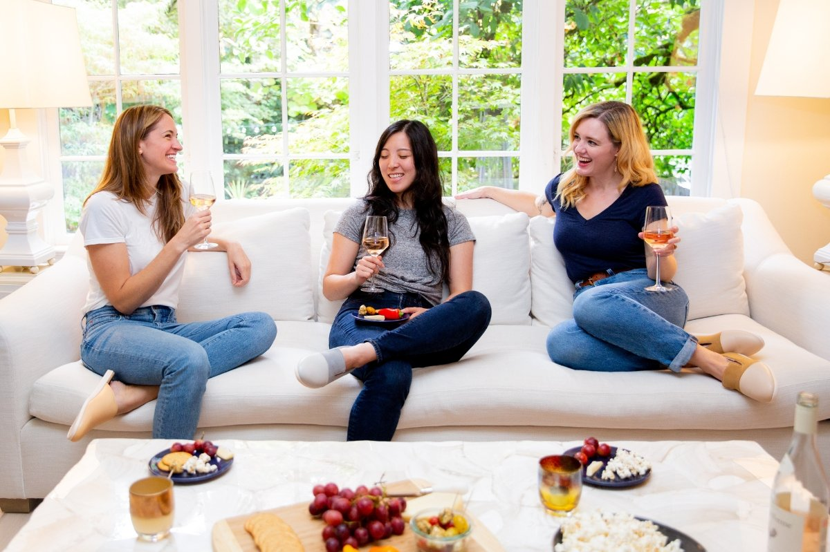 a group of women sitting on a couch with food and drinks