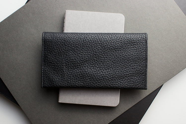 a black leather wallet on top of a grey notebook