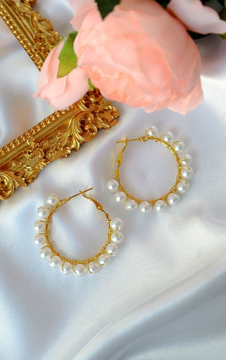 a pair of gold hoop earrings with pearls on a white cloth