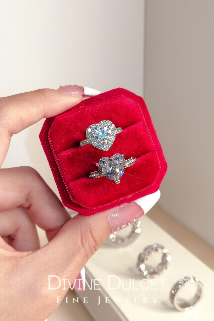 a hand holding a ring box with a heart shaped diamond ring