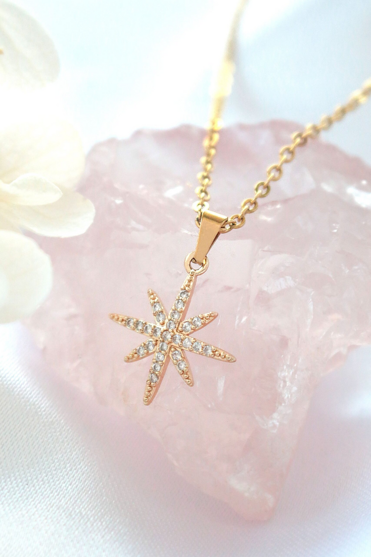 a gold necklace with a star shaped pendant on a pink surface