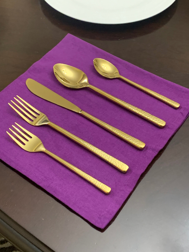 a gold spoon fork and knife on a purple napkin