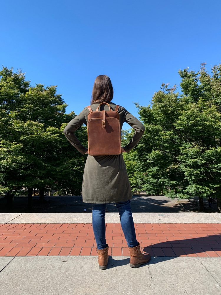a woman standing on a brick sidewalk with a brown backpack
