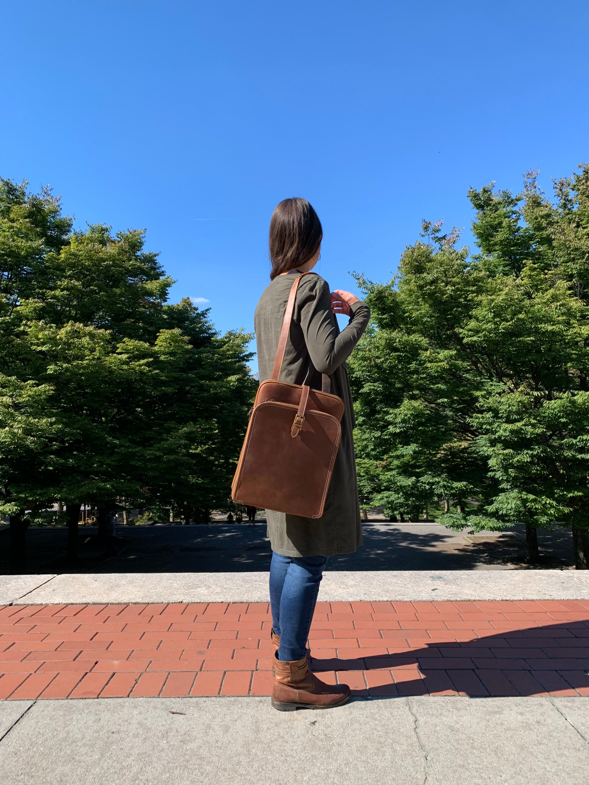 a woman standing on a brick walkway with a brown bag