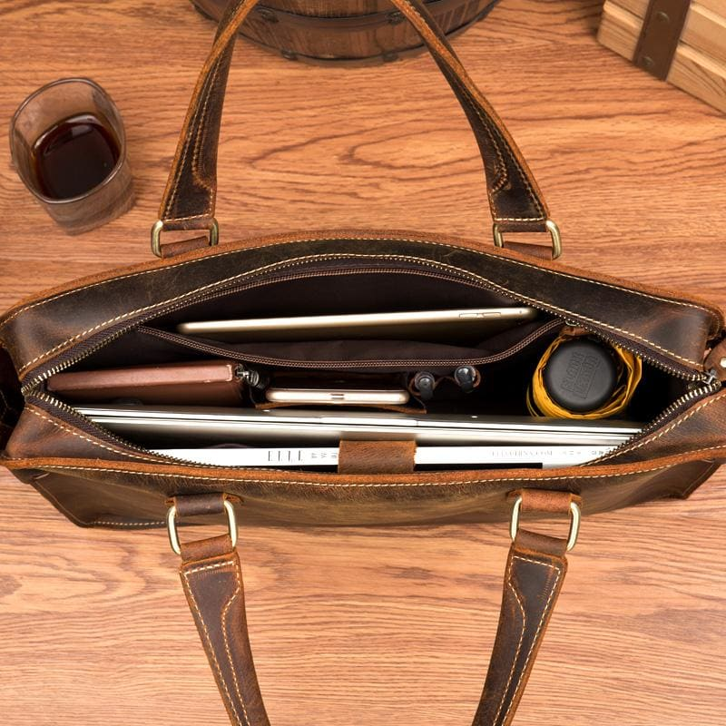 a brown leather bag with a glass of liquid and a bottle of liquid