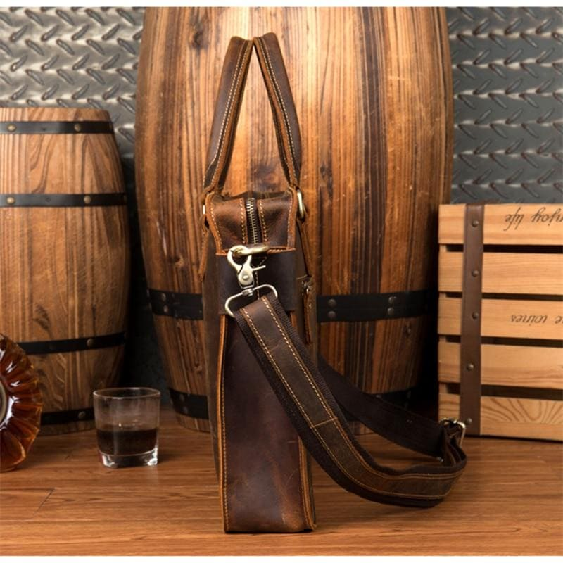 a brown leather bag with a strap and a glass of liquid next to it