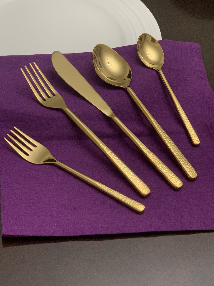 a gold spoon fork and knife on a purple napkin