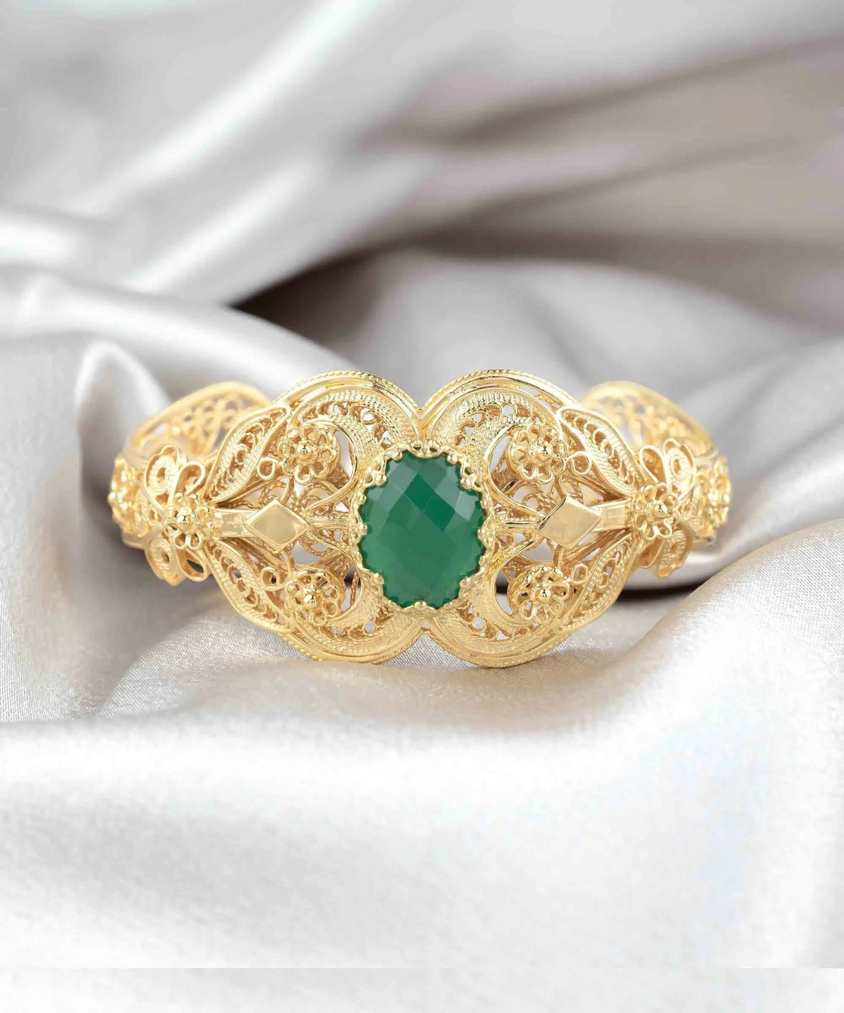 a gold ring with a green stone on a white fabric