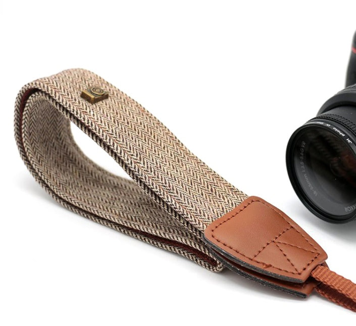 a camera strap with a brown strap and a black lens