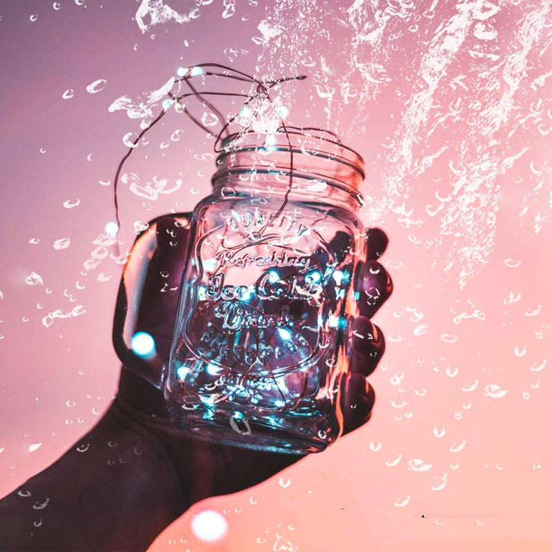 a hand holding a glass jar with lights coming out of it