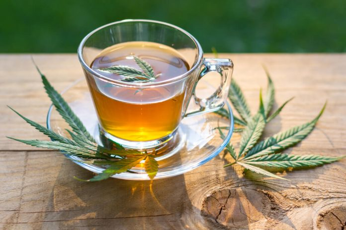 a glass cup of tea with leaves on a wooden surface