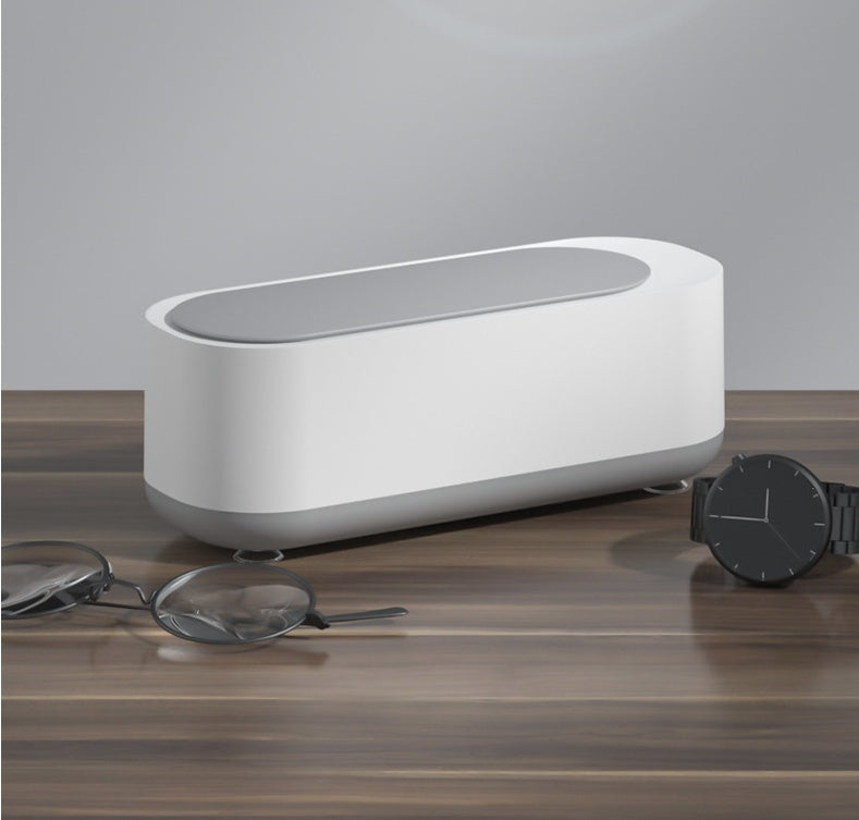 a white rectangular object with a black watch and glasses on a wooden surface