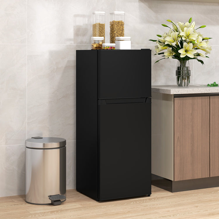 a black refrigerator with a flower vase and a trash can