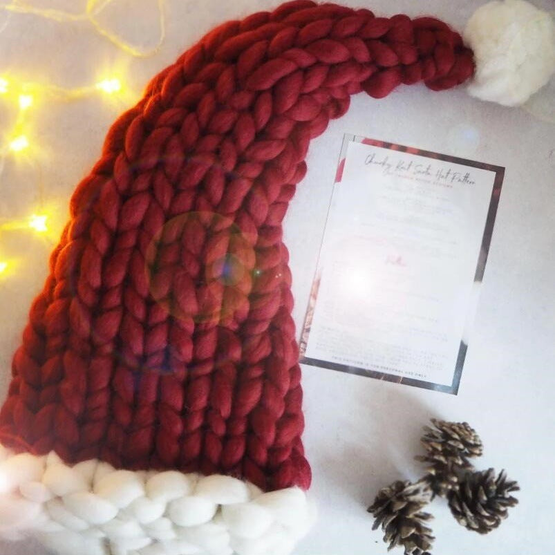 a red and white knit hat with a white and white pompom on a white surface