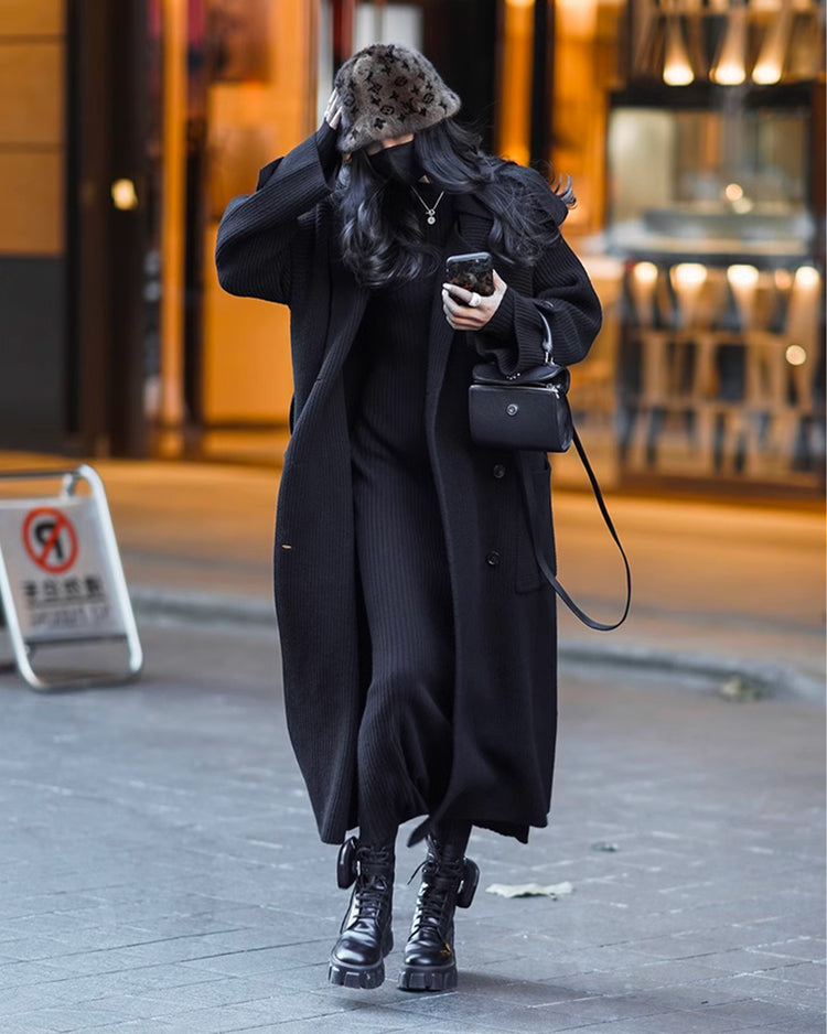 a woman in a black coat and hat walking down a street
