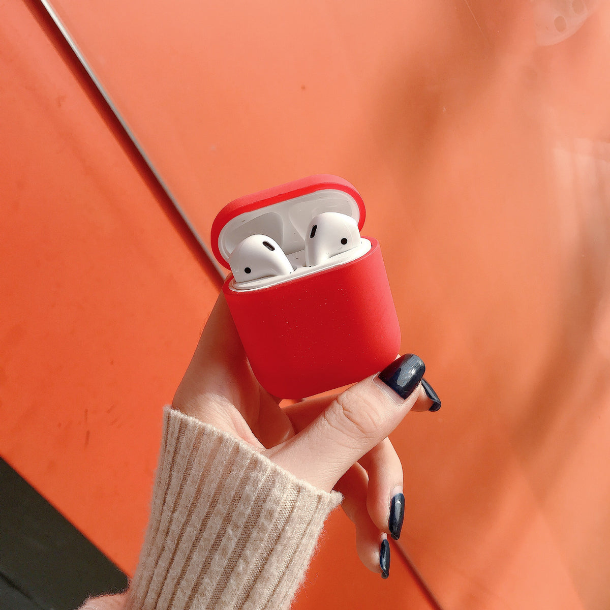 a hand holding a red case with white earbuds