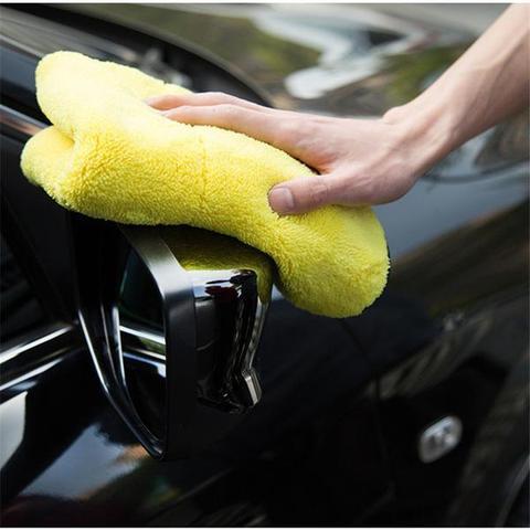 a hand holding a yellow microfiber cloth on a car mirror