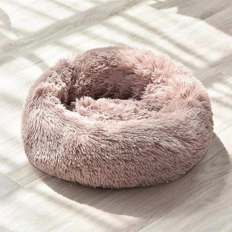 a round pink pet bed on a wood floor