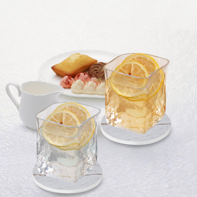 a pair of glasses with ice and lemons on a white table