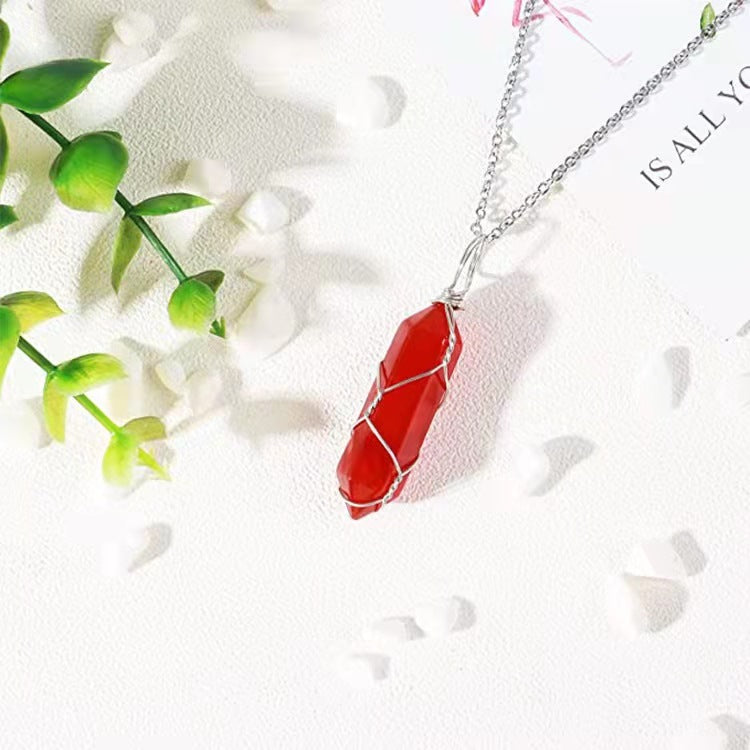 a red stone necklace on a silver chain next to a green plant