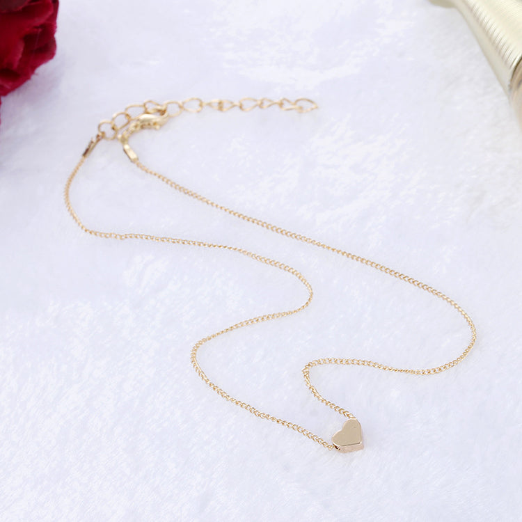 a gold heart necklace on a white surface next to a red rose